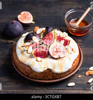 Torta di mandorle con fichi, panna montata e miele su sfondo di legno scuro, formato quadrato. Ricetta per dolci di stagione per le vacanze autunnali. Foto Stock