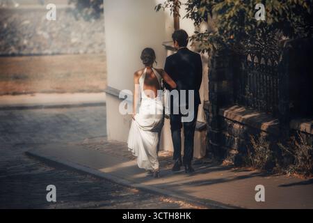 Sposa e sposo che camminano insieme in una giornata di sole, godendosi una romantica passeggiata in città. Foto Stock