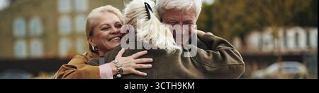 Intestazione di tre anziani caucasici che abbracciano all'aperto, sorridono e condividono momenti di gioia, due donne e un uomo che stanno vicini, mostrando affetto e felicità durante la riunione Foto Stock