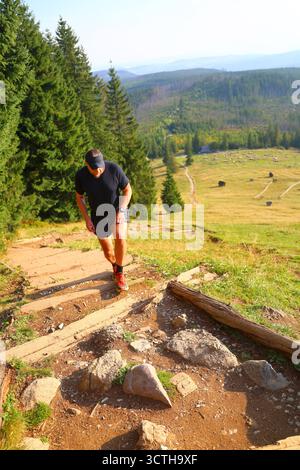 Uomo che corre su Hill su gradini nel paesaggio montuoso Foto Stock
