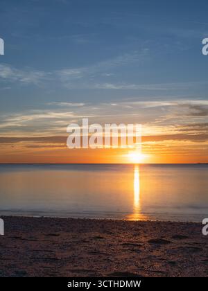 Il tranquillo tramonto illumina l'orizzonte marino, creando un perfetto riflesso dorato sulle acque tranquille Foto Stock