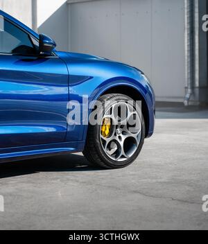 Ruota anteriore del SUV blu parcheggiata su una superficie in cemento. Vista ravvicinata di un'Alfa Romeo Stelvio con grandi cerchi e pneumatici sportivi. Foto Stock