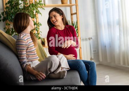 Felice madre incinta e figlia adolescente che hanno una piacevole conversazione, ridendo, chiacchierando a casa Foto Stock