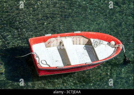 La barca rossa galleggia dolcemente in acque calme e limpide vicino alla costa rocciosa sotto il sole luminoso. Foto Stock