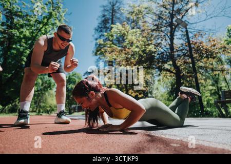 Donna esegue push-up all'aperto mentre viene incoraggiata dal suo allenatore di fitness Foto Stock