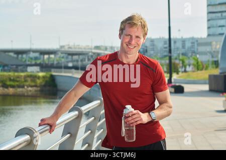 Il giovane sorride mentre si riposa dopo l'allenamento all'aperto Foto Stock