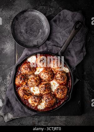 Primo piano di polpette al forno in ricca salsa di pomodoro con mozzarella fusa, fotografate in una luce soffusa e suggestiva per temi rustici e di comfort. Foto Stock