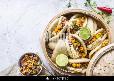 Soffici panini bao al vapore ripieni di halloumi grigliati e vivace salsa di mango con lime ed erbe aromatiche in una vaporiera di bambù. Foto Stock