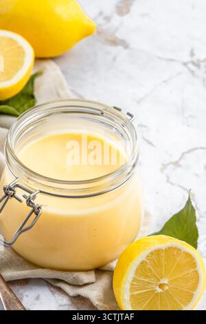 Liscia la cagliata di limone fatta in casa in un vaso di vetro con limoni freschi su una superficie in marmo e con luce naturale brillante. Foto Stock