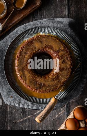 Budino di spugna di sciroppo dorato appiccicoso in una sagoma ad anello con glassa al caramello su un tavolo di legno scuro per un dolce accogliente. Foto Stock