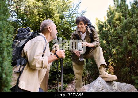 Una coppia di anziani affettuosa condivide un momento mentre cammina attraverso la vegetazione lussureggiante delle montagne. Foto Stock