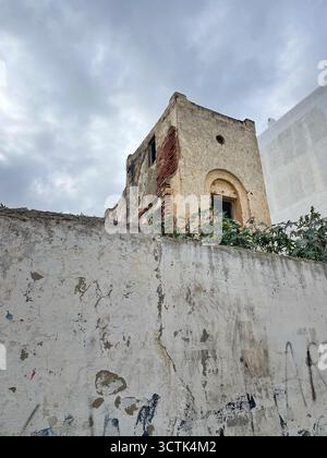 Facciata sbriciolata e finestra rotta dietro muro macchiato con graffiti, Martil, Tetouan, Marocco, 6 ottobre 2025. Foto Stock