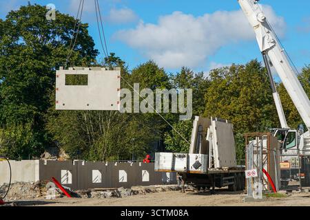 La grande gru solleva pannelli in calcestruzzo prefabbricato nel cantiere di edifici residenziali a più piani, utilizzando metodi moderni per l'assemblaggio dell'edificio Foto Stock