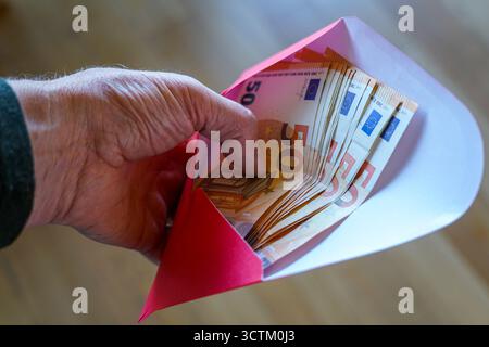 Primo piano di una mano che detiene una busta piena di banconote da 50 euro, che simboleggia risparmi, stipendi, pensioni, aiuti finanziari, pagamento in contanti o regalo Foto Stock