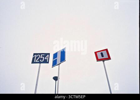 Tre segnali stradali sull'acqua contro un cielo nuvoloso, catturati da un angolo basso su pellicola analogica. Foto Stock