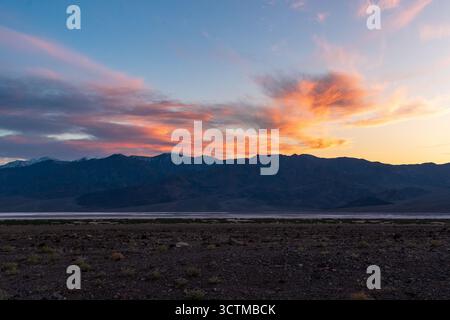Tramonto sul bacino di Badwater, la Valle della morte, con le scintillanti montagne Panamint e un terreno incruso di sale modellato dal tempo e dalla geologia del deserto. Foto Stock