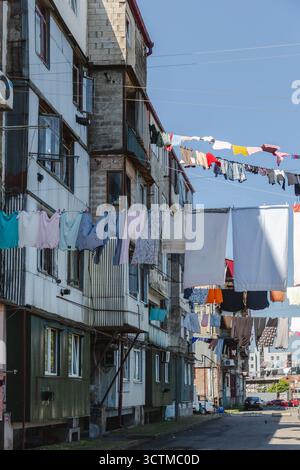 Vista delle colorate linee di lavanderia disposte attraverso una stretta strada sotto edifici antichi sotto un cielo luminoso, Batumi, Adjara, Georgia. Foto Stock