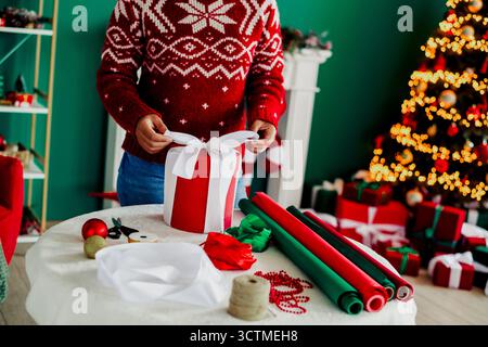 Scena festiva di un regalo avvolto in un accogliente interno natalizio con albero e decorazioni, che mostra gioia di preparazione per le vacanze Foto Stock