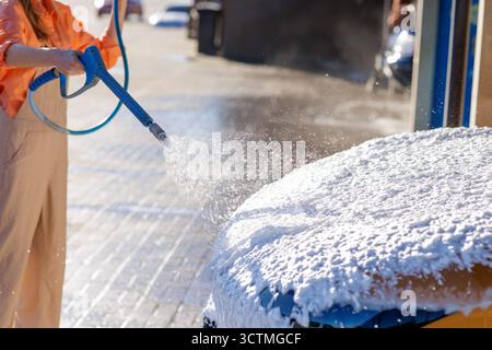 L'idropulitrice a pressione Closeup spruzza schiuma spessa sul cofano di un'auto in un lavaggio self-service, perfetta per la cura automatica, i dettagli e i temi di pulizia fai da te Foto Stock