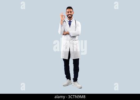 Allegro maschio arabo gesto del dottore Okay Sign Over Blue background Foto Stock