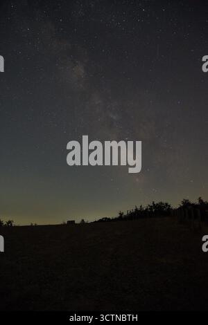 Cielo stellato notturno con la via Lattea visibile sopra un paesaggio rurale scuro. Visuale chiara di innumerevoli stelle e fasce di polvere cosmiche, catturate in condizioni di scarsa illuminazione Foto Stock