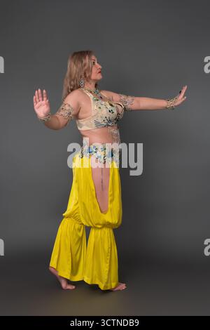 Vista del profilo di una donna caucasica con le braccia allungate che indossa un abito da ballo - top e pantaloni harem gialli e non indossa scarpe stantidi Foto Stock