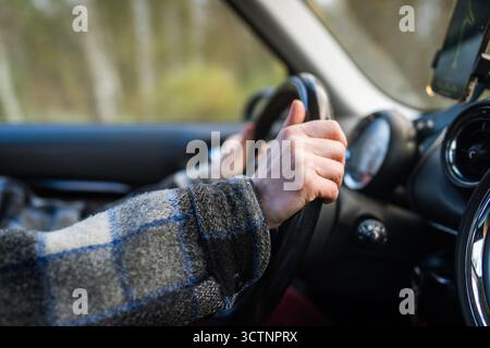 Primo piano di una donna che tiene le mani al volante e guida un'auto, utilizzando l'app di navigazione sullo smartphone. Foto Stock