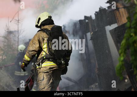 Un vigile del fuoco professionista con casco e tuta protettiva in piedi nel fitto fumo sul luogo del fuoco Foto Stock
