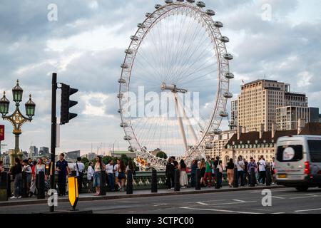 Londra, Regno Unito 09 luglio 2025 Vista serale del London Eye dal Westminster Bridge sul Tamigi con persone che camminano e auto che passano Foto Stock