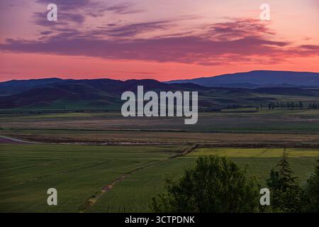 Tramonto su colline ondulate e terreni agricoli. Paesaggio panoramico caratterizzato da lussureggianti campi agricoli verdi in primo piano. Colline ondulate. Foto Stock