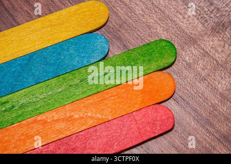 Bastoncini di legno colorati posti in fila su una superficie di legno. I bastoncini sono dipinti in giallo, blu, verde, arancione e rosso. Per un look brillante e divertente Foto Stock