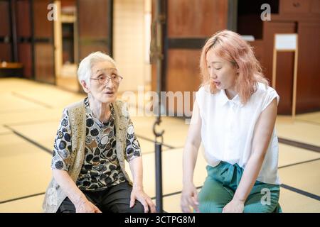 Una donna con i capelli rosa si siede accanto a una donna più anziana. La donna più anziana indossa occhiali e un giubbotto. Le due donne parlano tra loro Foto Stock