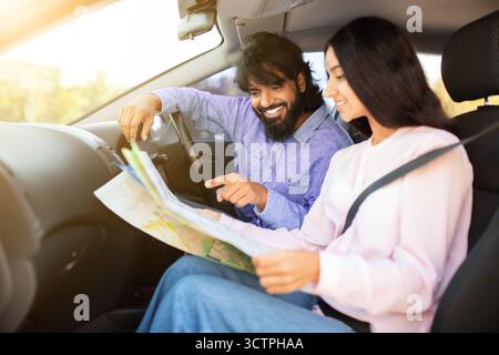 Felice coppia indiana dentro auto che legge la mappa insieme, che punta e sorride Foto Stock