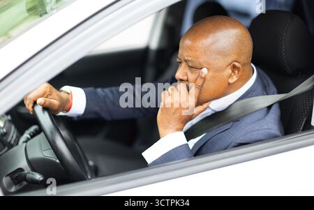 Uomo d'affari afroamericano maturo che guida un'auto e riposa la testa a portata di mano Foto Stock