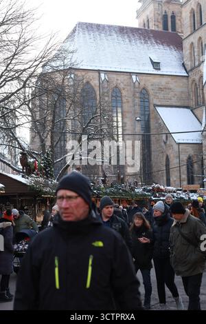 Stoccarda, Germania - 18 dicembre 2022, i visitatori passeggiano attraverso un tradizionale mercatino di Natale adagiato contro una cattedrale storica, con tetti innevati e. Foto Stock
