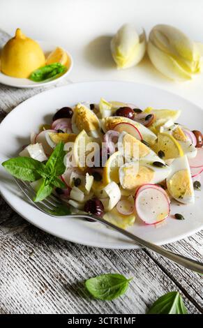 Insalata fresca con indivia, uova sode, ravanello, cipolla, olive, semi di limone e girasole su un piatto su fondo di legno. Vista dall'alto. Foto Stock