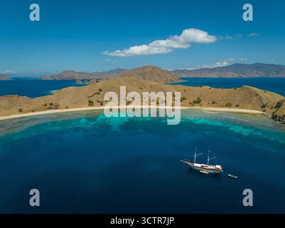 Foto con drone di uno yacht subacqueo ormeggiato in una splendida baia, acque azzurre tropicali e isole Komodo sullo sfondo. Komodo, Indonesia Foto Stock
