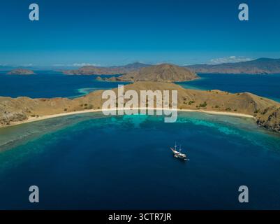 Foto con drone di uno yacht subacqueo ormeggiato in una splendida baia, acque azzurre tropicali e isole Komodo sullo sfondo. Komodo, Indonesia Foto Stock