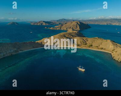 Foto con drone di uno yacht subacqueo ormeggiato in una splendida baia, acque azzurre tropicali e isole Komodo sullo sfondo. Komodo, Indonesia Foto Stock