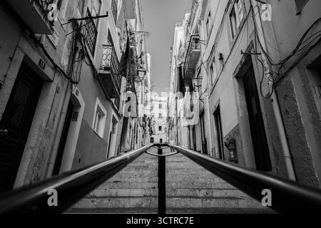 Strada stretta bianca e nera con scale in pietra e balconi nella città vecchia di Lisbona - architettura urbana e atmosfera storica Foto Stock