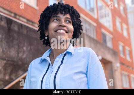 Giovane donna nera sorridente mentre si trova all'aperto in un ambiente urbano. Foto Stock