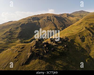 Vista aerea delle antiche abitazioni in pietra annidate nelle aspre pendici soleggiate delle montagne del Caucaso, le erbe dorate contrastano con le pietre scure, Dartlo, Kakheti, Georgia. Foto Stock