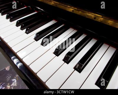 Vista laterale ravvicinata dei tasti piano in bianco e nero lucido con il riflesso del bordo in ottone dorato da un angolo basso con una profondità di campo ridotta. Foto Stock