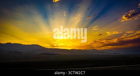 Spettacolare tramonto dorato con raggi di luce che brillano su una catena montuosa lontana, creando un paesaggio sereno e suggestivo. Foto Stock