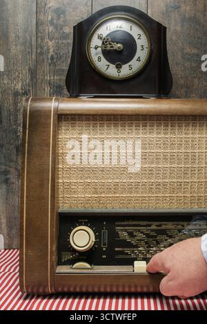 Autentica radio retrò e orologio da tavolo. Verticale. La mano di un uomo accende il pulsante sulla radio Foto Stock