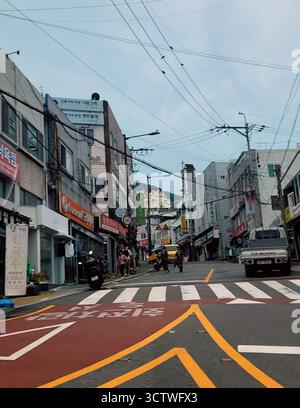 Una fotografia di una scena di strada a Busan, Corea del Sud, che mostra un vivace paesaggio urbano sotto un cielo coperto. Busan, situata sulla costa sud-orientale della penisola coreana, è la seconda città più popolosa della Corea del Sud dopo Seul ed è un'importante città portuale. Il suo paesaggio urbano è caratterizzato da un mix di alti edifici moderni e quartieri più vecchi e densamente affollati, spesso costruiti su colline a causa del terreno montuoso della città. 2025. Foto Stock