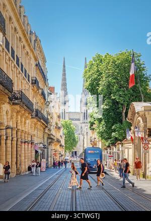 Bordeaux, Francia - 10 maggio 2024: Vista sulla strada verso le torreggianti guglie della Cattedrale di Saint-Andre. Eleganti edifici in pietra fiancheggiano la strada pedonale Foto Stock