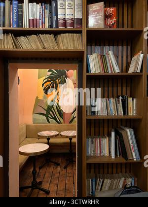 L'immagine mostra un angolo di un caffè o libreria con scaffali di legno pieni di libri e riviste. Attraverso un'apertura negli scaffali, una piccola se Foto Stock