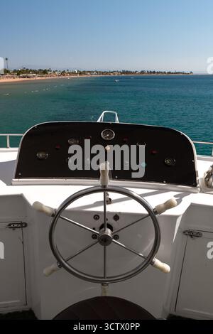Una splendida vista dal ponte dello yacht del mare turchese e della costa, con il volante della barca e il pannello di controllo con sensori visibili. Foto Stock