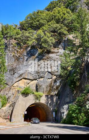 Tunnel Entrance Road and Car circondato dalle scogliere rocciose e dalla lussureggiante Green Forest Foto Stock